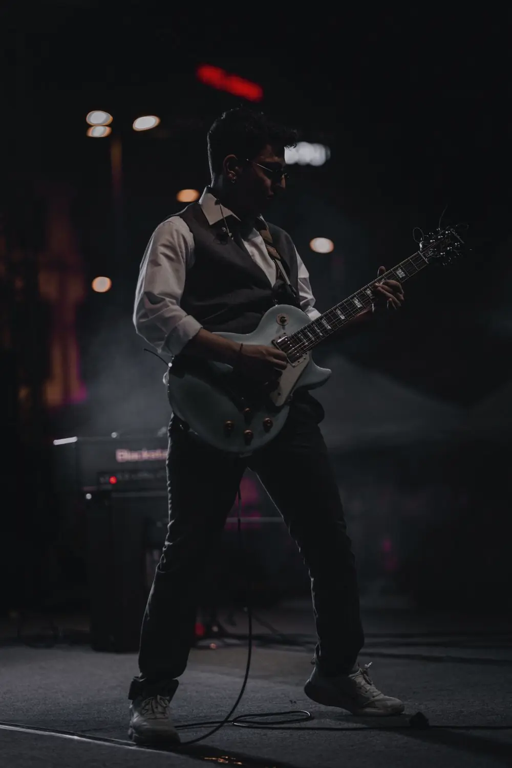 Mehmet in silhouette mid-song on a dark stage, guitar cable trailing across the floor.